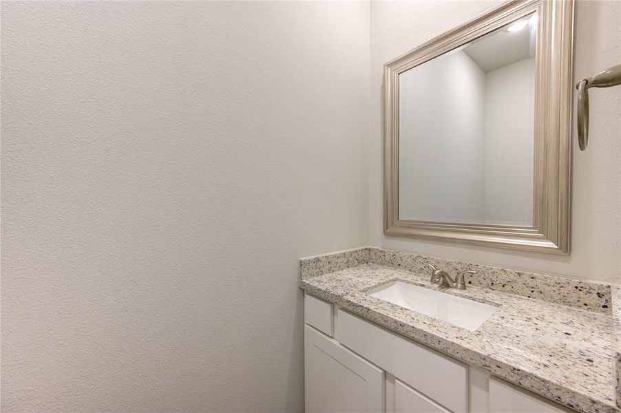 Powder bath for your guests with granite counters & framed mirror.