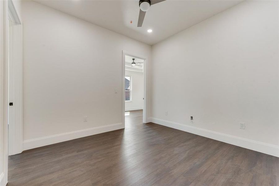 Spacious interior room featuring wood-finish flooring, white baseboards, and a modern ceiling fan Spacious interior room featuring wood-finish flooring, white baseboards, and a modern ceiling fan