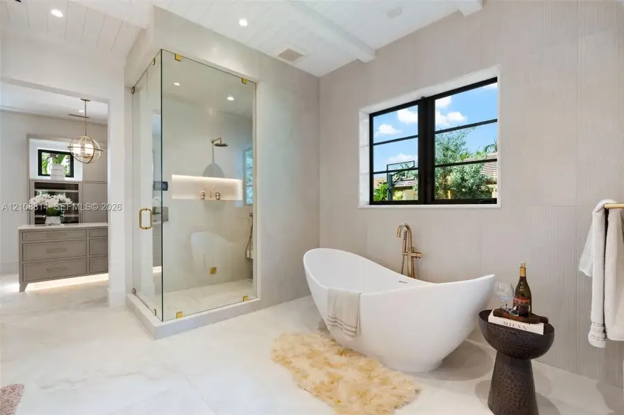 Freestanding soaking tub with a wall-mounted faucet, glass-enclosed shower featuring built-in shelving, large-format tile flooring, and plank-style ceiling detailing Freestanding soaking tub with a wall-mounted faucet, glass-enclosed shower featuring built-in shelving, large-format tile flooring, and plank-style ceiling detailing
