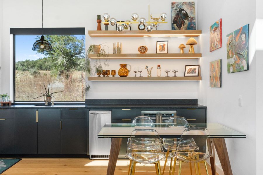 Contemporary kitchen featuring a large window, dark cabinetry with brass hardware, a built-in beverage refrigerator, illuminated open shelving, and wood-finish flooring