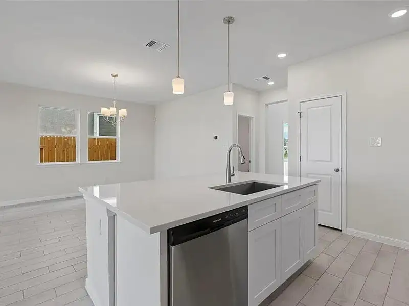A pristine white kitchen island with modern pendant lights anchors this inviting open-concept living space.