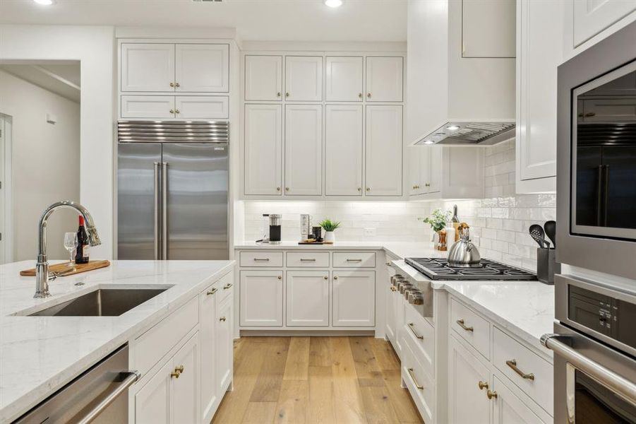 Kitchen with sink, custom exhaust hood, white cabinetry, light stone counters, and stainless steel appliances