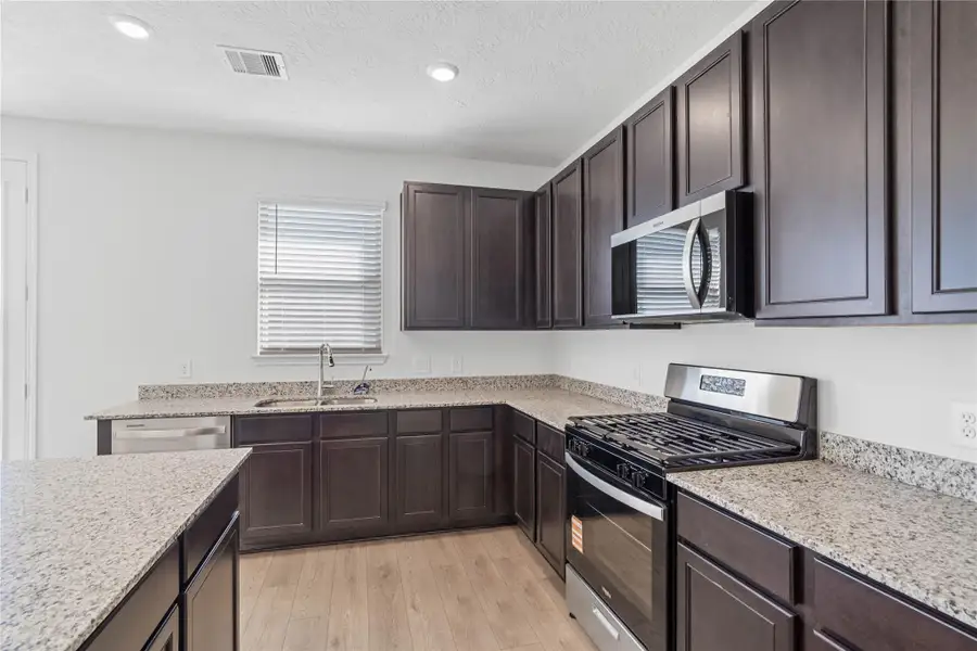 A true chef’s dream, this expansive kitchen boasts high ceilings, rich Woodmont Belmont cabinetry in an Espresso stain, Granite countertops in Luna Pearl, stainless steel appliances, a modern tile backsplash, recessed lighting, extended counter space, an island, and a walk-in pantry—all with a clear view of the spacious family room.