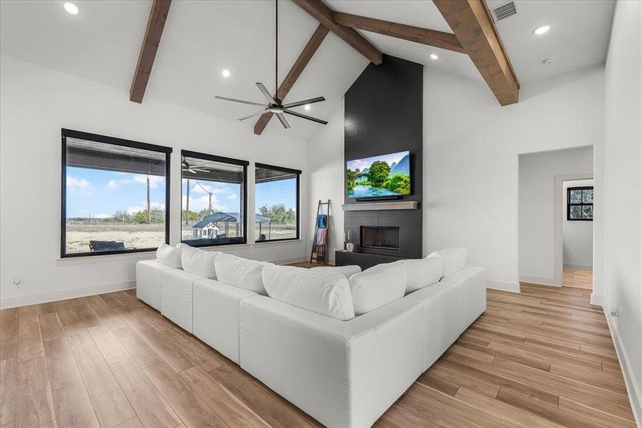 Living room featuring beam ceiling, ceiling fan, a fireplace, and high vaulted ceiling