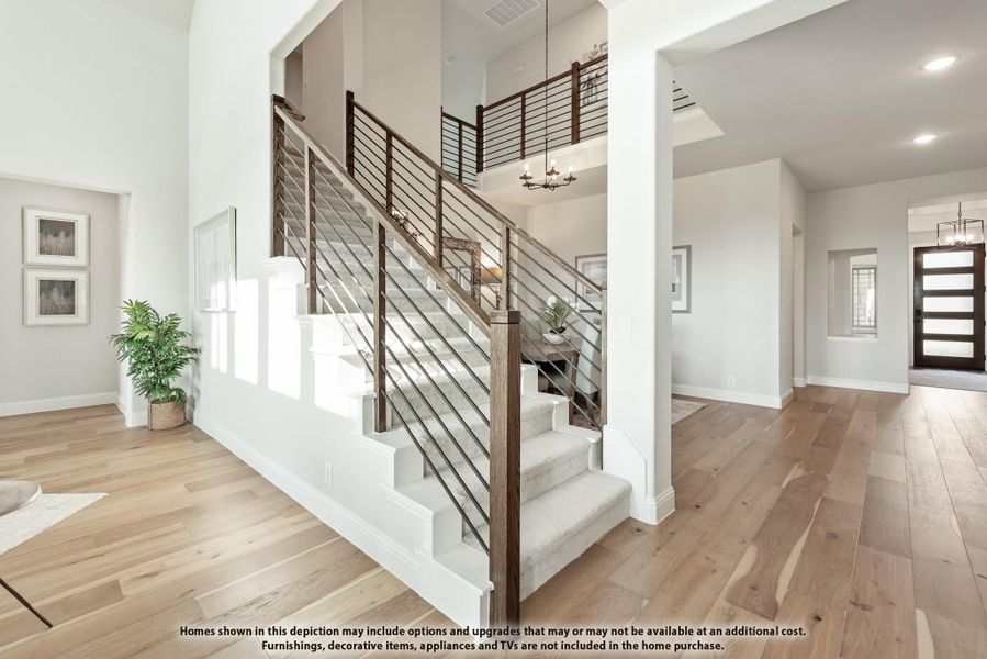Two-story foyer with open staircase, wood and metal railing, hardwood floors, and front entry door visible in background. Two-story foyer with open staircase, wood and metal railing, hardwood floors, and front entry door visible in background.
