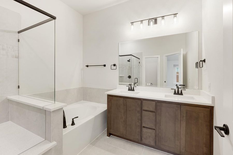 Bathroom with double sink vanity, soaking tub, glass shower, and dark wood cabinets with white countertops