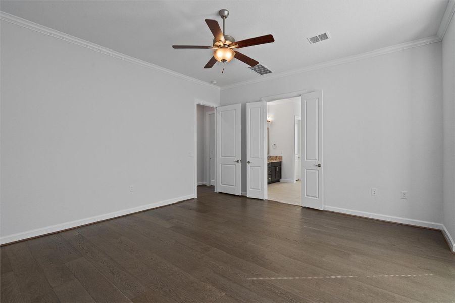 Unfurnished bedroom featuring crown molding, ceiling fan, dark wood-style flooring, and ensuite bath Unfurnished bedroom featuring crown molding, ceiling fan, dark wood-style flooring, and ensuite bath
