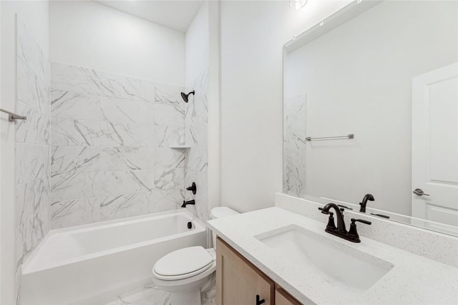 Bathroom with marble-tile tub surround, white quartz vanity, dark bronze fixtures, and large mirror