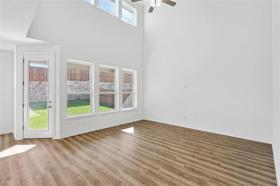 Unfurnished room with a wealth of natural light, ceiling fan, a towering ceiling, and hardwood / wood-style flooring