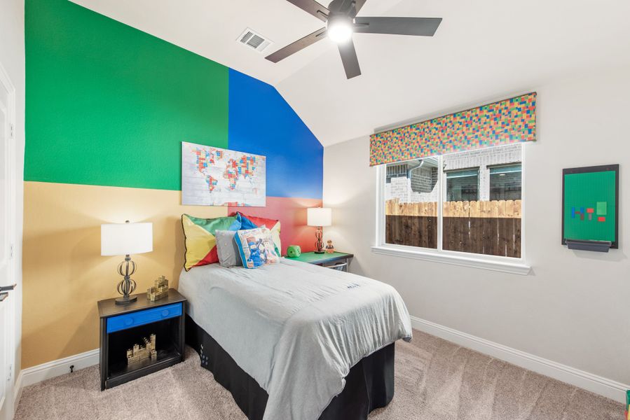 Children's bedroom with colorful block-themed accent wall, twin bed, ceiling fan, and carpet flooring Children's bedroom with colorful block-themed accent wall, twin bed, ceiling fan, and carpet flooring