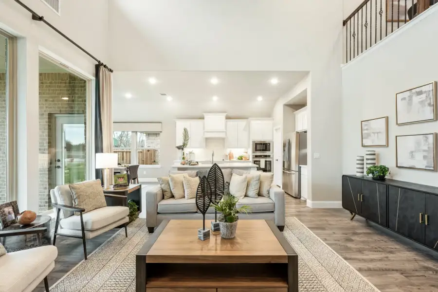 Open-concept living room with high ceilings, hardwood floors, and kitchen visible in background