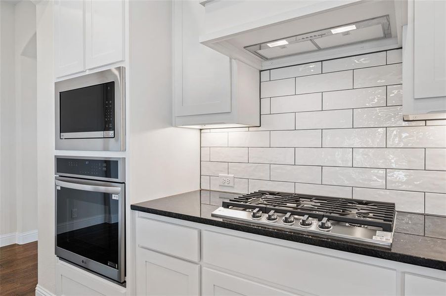 Kitchen featuring range hood, stainless steel appliances, white cabinets, and dark stone counters Kitchen featuring range hood, stainless steel appliances, white cabinets, and dark stone counters