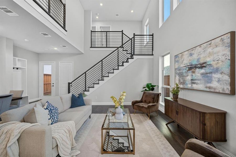 Two-story living area featuring beautiful wood-finish flooring, a contemporary staircase with black railings, and an open-concept upper-level balcony