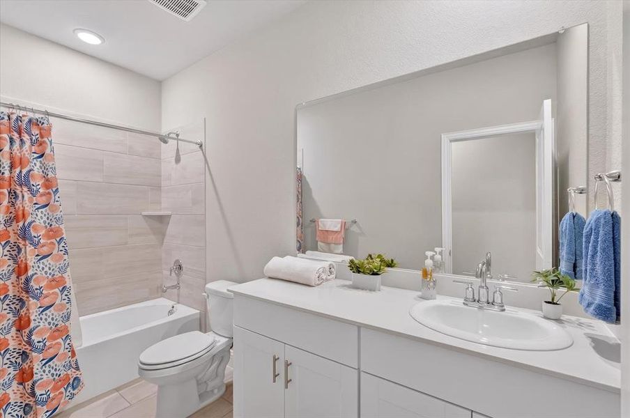 Bathroom featuring a white vanity with an undermount sink, a large wall-mounted mirror, a built-in tub with a shower, and light-toned horizontal tile surrounding the tub Bathroom featuring a white vanity with an undermount sink, a large wall-mounted mirror, a built-in tub with a shower, and light-toned horizontal tile surrounding the tub