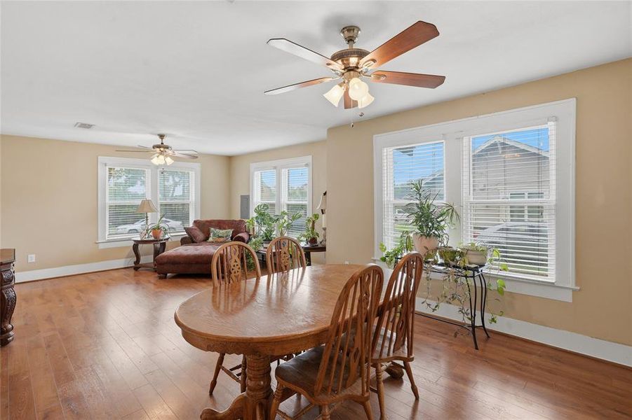 Open-concept living space featuring wood-finish flooring, multiple windows, and two ceiling fans with integrated lighting