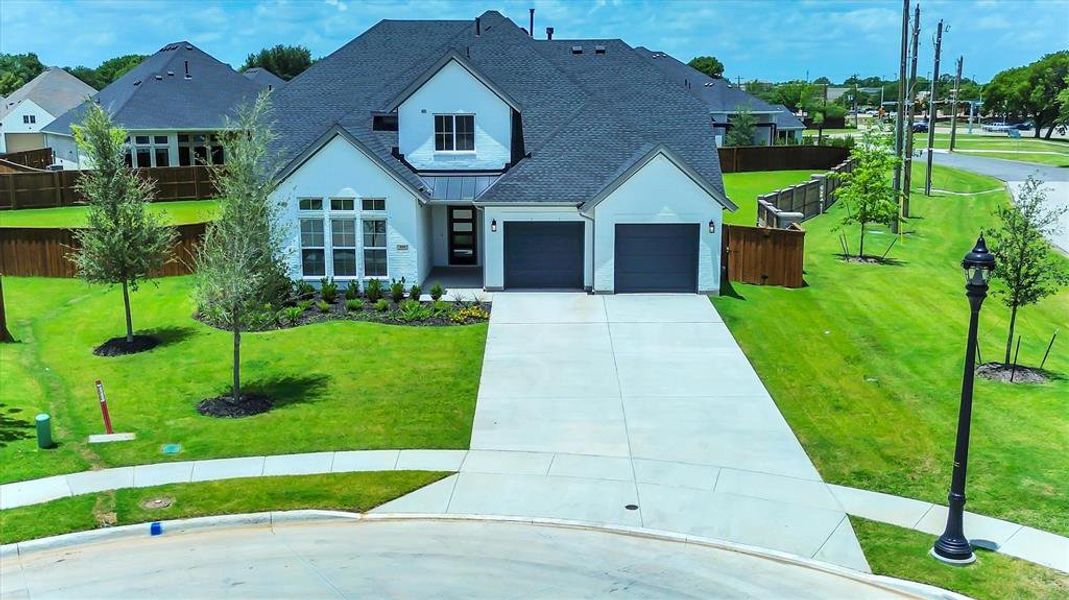 Modern white stucco exterior with a dark shingle roof, featuring a two-car garage, a concrete driveway, and established landscaping Modern white stucco exterior with a dark shingle roof, featuring a two-car garage, a concrete driveway, and established landscaping