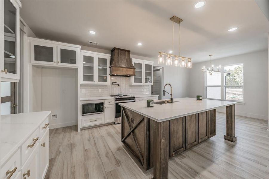 Kitchen featuring glass insert cabinets, white cabinetry, stainless steel range, custom exhaust hood, and decorative light fixtures