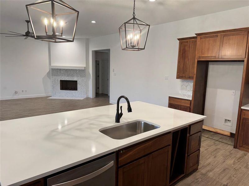 Kitchen featuring decorative light fixtures, tasteful backsplash, sink, a tiled fireplace, and stainless steel dishwasher