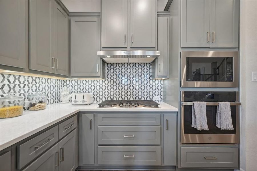 Kitchen featuring gray cabinetry, backsplash, stainless steel appliances, and exhaust hood