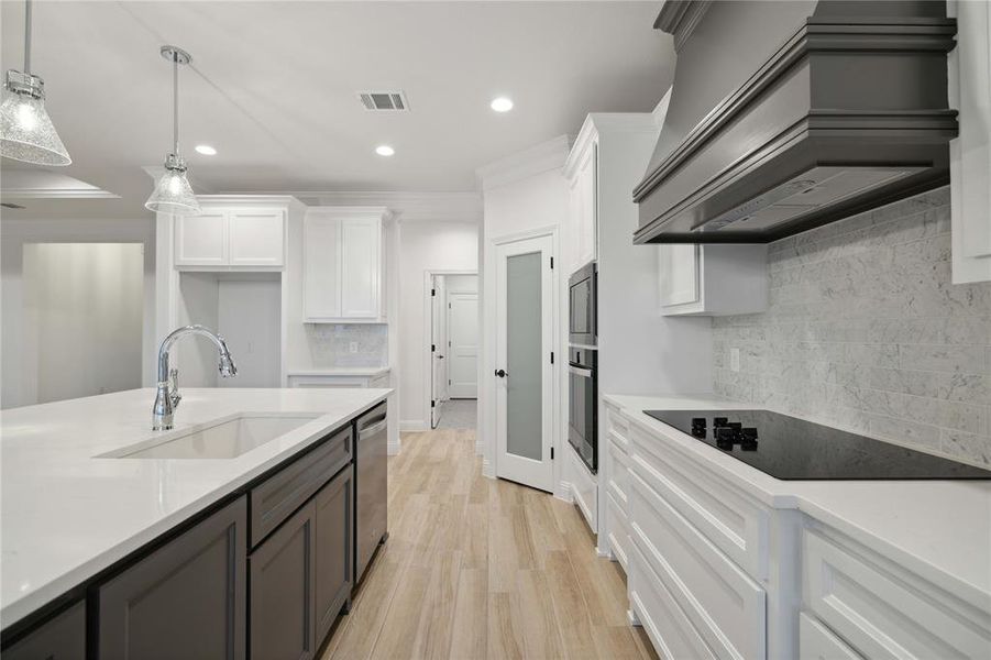 Kitchen featuring white cabinetry, custom range hood, appliances with stainless steel finishes, and sink