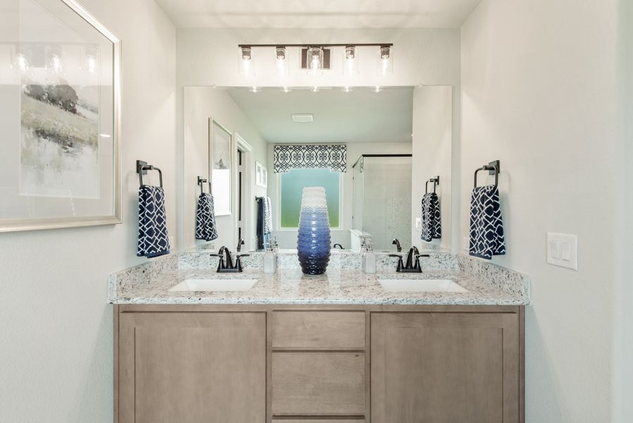 Bathroom with double sink vanity, granite countertop, wood cabinets, and large mirror with overhead lighting