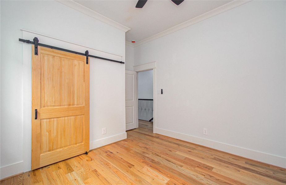 This bright secondary bedroom features hardwood floors, two large windows for natural light, and a stylish sliding barn door.