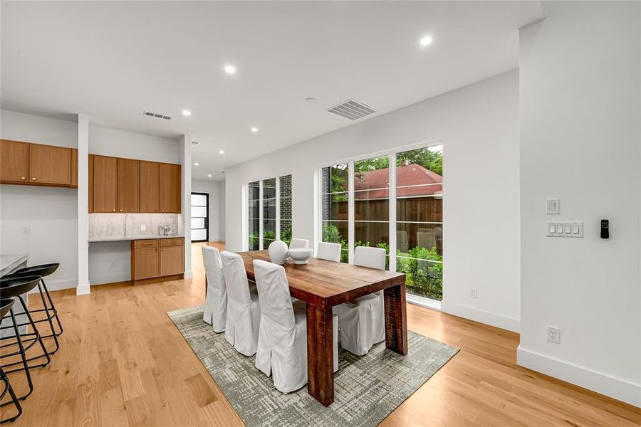 Open-concept dining area featuring large windows, wood-finish flooring, recessed lighting, and a built-in buffet with light wood cabinetry and a stone backsplash