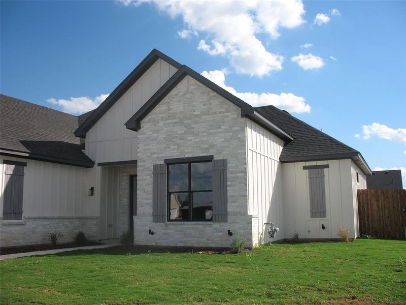 View of front facade featuring board and batten siding, brick siding, and a shingled roof
