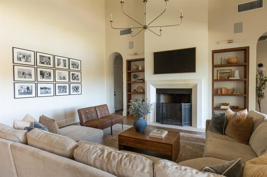 Living room with built in shelves, arched walkways, a fireplace, a high ceiling, and suspended lighting