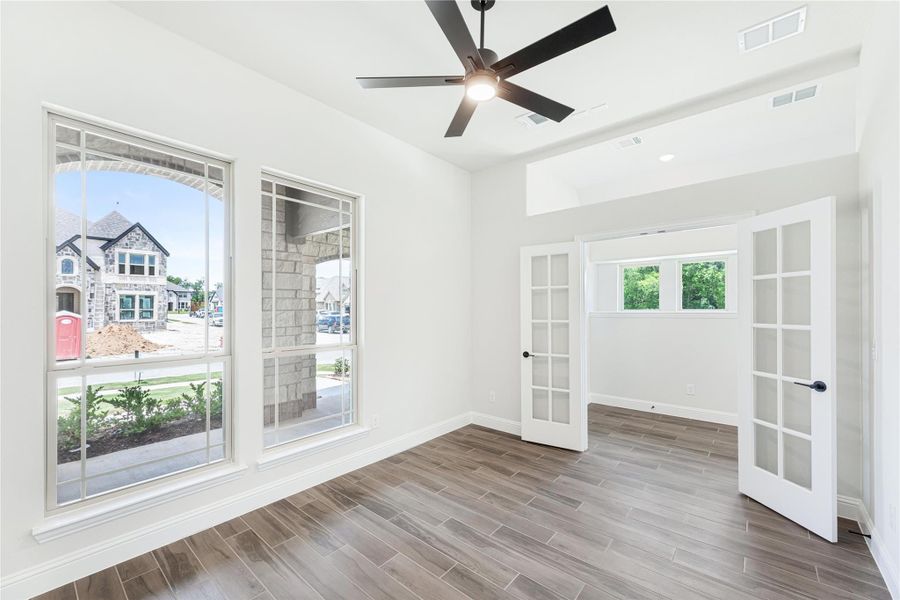 Empty room with wood-look tile floors, ceiling fan, large windows, and French doors with frosted glass panels Empty room with wood-look tile floors, ceiling fan, large windows, and French doors with frosted glass panels