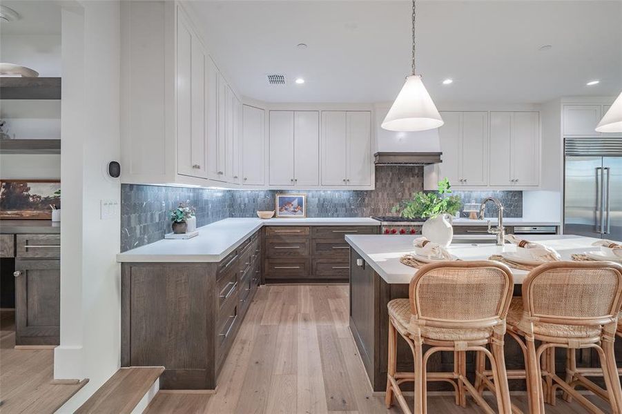 Kitchen with decorative backsplash, a center island with sink, white cabinetry, light hardwood / wood-style floors, and stainless steel appliances