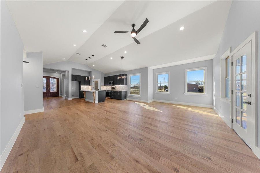 Unfurnished living room with french doors, lofted ceiling, light wood finished floors, recessed lighting, and a ceiling fan Unfurnished living room with french doors, lofted ceiling, light wood finished floors, recessed lighting, and a ceiling fan