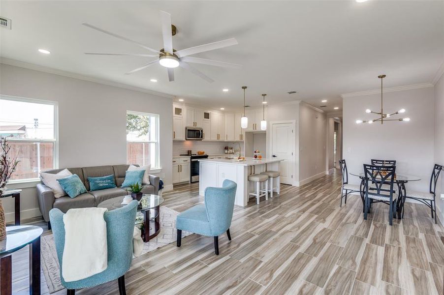 Living room with light hardwood / wood-style floors, ceiling fan with notable chandelier, and ornamental molding