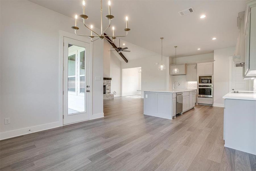 Kitchen featuring light wood-type flooring, a stone fireplace, a center island with sink, lofted ceiling, and stainless steel appliances