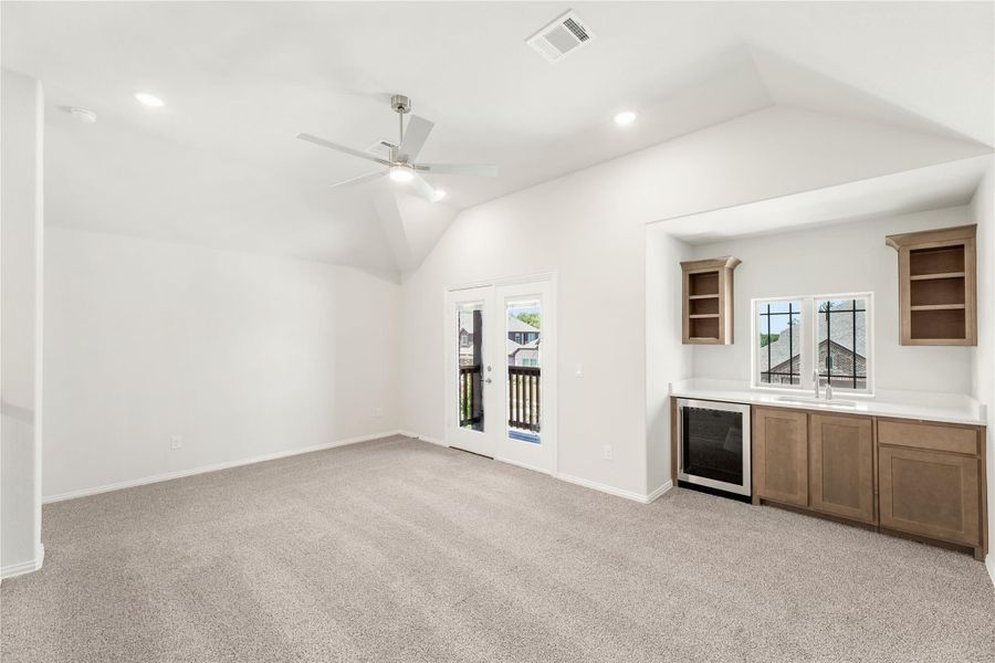 Bonus room with vaulted ceiling, ceiling fan, wet bar with wood cabinets, and French doors to balcony