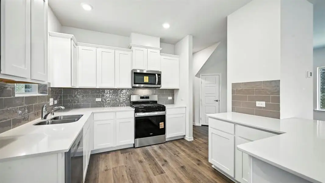 Kitchen featuring appliances with stainless steel finishes, white cabinetry, dark wood finished floors, light stone countertops, and backsplash