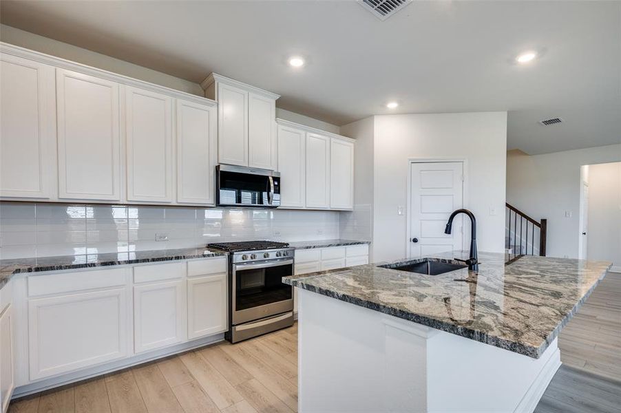 Kitchen with stainless steel appliances, tasteful backsplash, dark stone countertops, white cabinets, and light wood-style flooring Kitchen with stainless steel appliances, tasteful backsplash, dark stone countertops, white cabinets, and light wood-style flooring