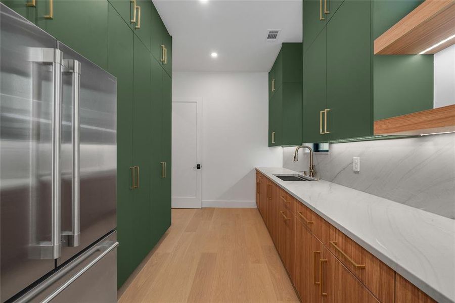 Kitchen featuring high end refrigerator, light stone countertops, light wood-style flooring, modern cabinets, and green cabinetry Kitchen featuring high end refrigerator, light stone countertops, light wood-style flooring, modern cabinets, and green cabinetry