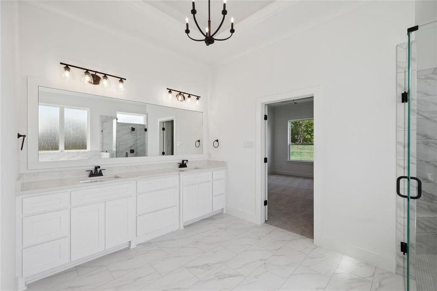 Bathroom featuring tile patterned flooring, double sink vanity, a shower with door, a chandelier, and a tray ceiling