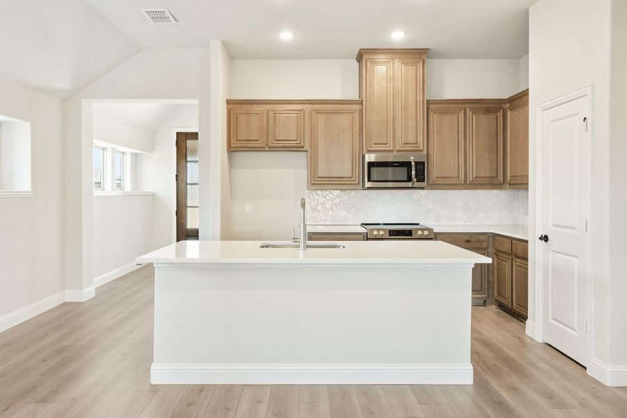Kitchen with large white island, tan wood cabinets, stainless appliances, and light hardwood floors Kitchen with large white island, tan wood cabinets, stainless appliances, and light hardwood floors