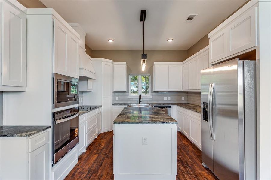 Kitchen featuring stainless steel appliances, dark stone countertops, dark wood finished floors, pendant lighting, and a center island Kitchen featuring stainless steel appliances, dark stone countertops, dark wood finished floors, pendant lighting, and a center island
