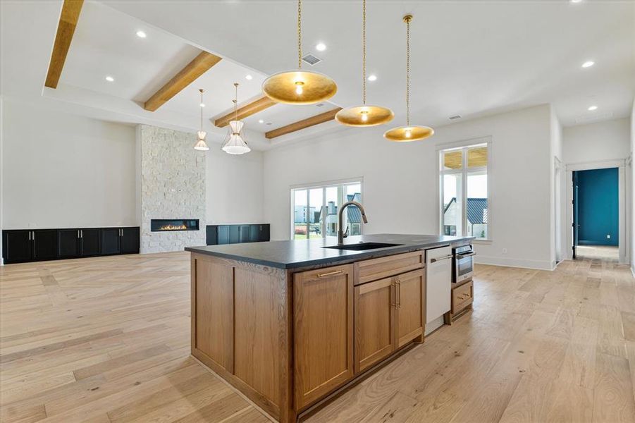 Kitchen with dark countertops, an island with sink, brown cabinets, beam ceiling, and light wood-type flooring