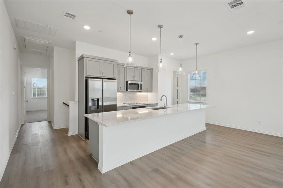 Kitchen with gray cabinetry, a kitchen island with sink, hanging light fixtures, sink, and appliances with stainless steel finishes