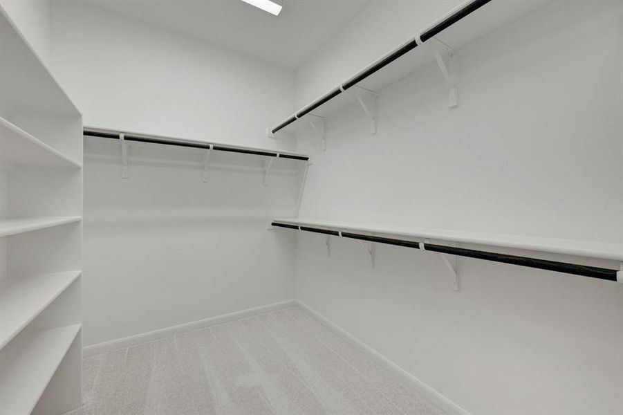 Spacious walk-in closet featuring built-in shelving, multiple hanging rods, light-colored carpet, and recessed ceiling lighting Spacious walk-in closet featuring built-in shelving, multiple hanging rods, light-colored carpet, and recessed ceiling lighting
