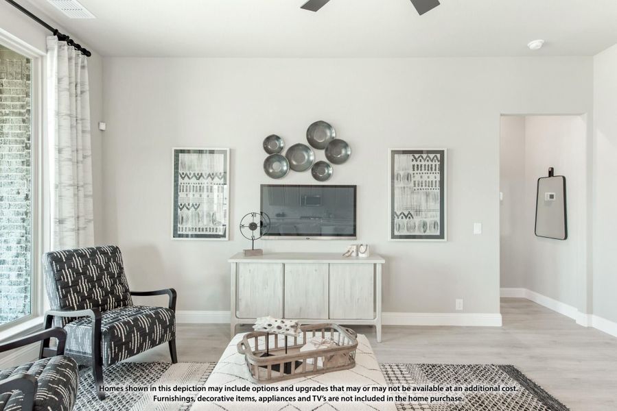 Living room with light wood floors, ceiling fan, TV on white console, and patterned accent chair near large window Living room with light wood floors, ceiling fan, TV on white console, and patterned accent chair near large window
