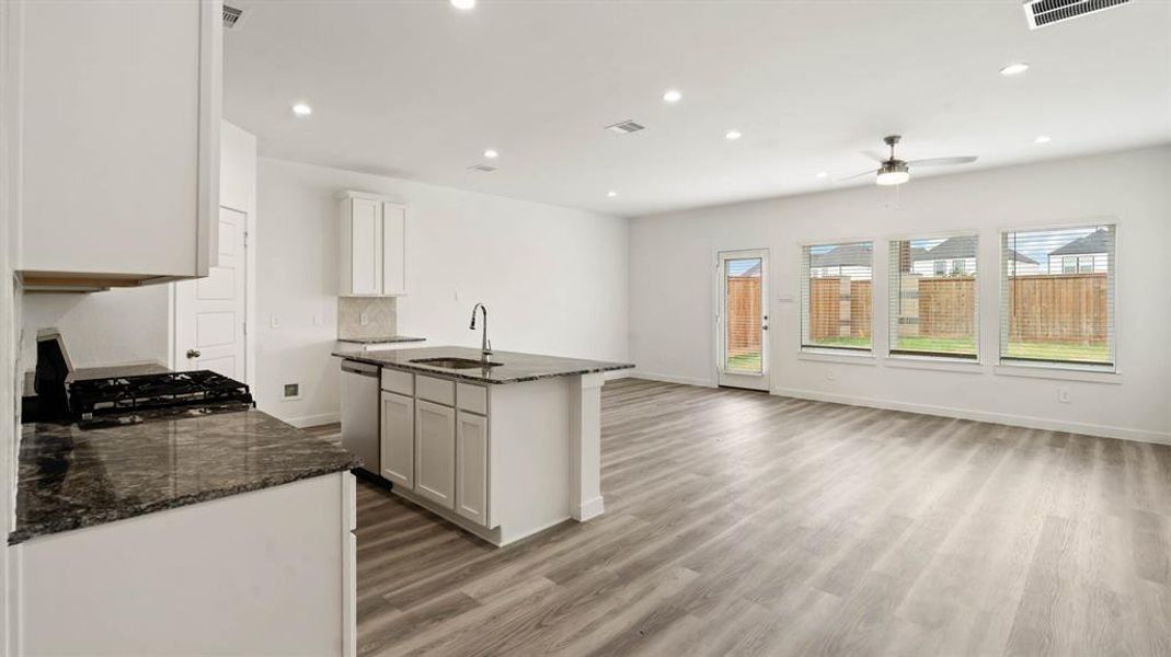 Kitchen featuring dark stone countertops, recessed lighting, a center island with sink, white cabinetry, and light wood-style flooring