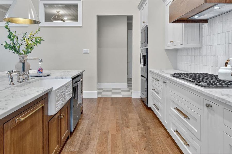 Kitchen featuring white cabinets, light stone counters, light wood finished floors, appliances with stainless steel finishes, and custom range hood