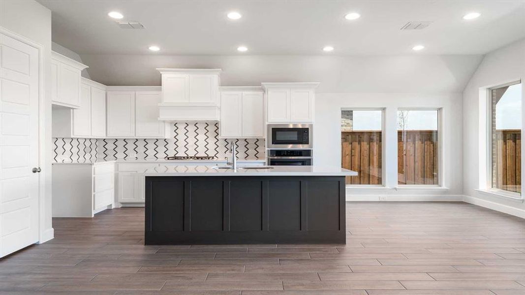 Kitchen with hardwood / wood-style floors, oven, lofted ceiling, a center island with sink, and white cabinets