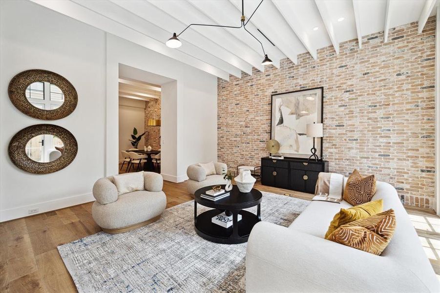 The beamed ceilings and neutral designer wall paint create a harmonious and elegant living space, complemented by a striking brick feature wall. This area offers seamless access to the kitchen and dining room, enhancing both functionality and aesthetic appeal.