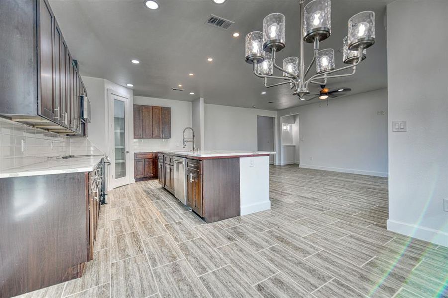 Kitchen featuring appliances with stainless steel finishes, sink, decorative light fixtures, decorative backsplash, and a center island with sink